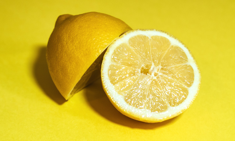 Closeup of a lemon cut in half resting on a yellow counter to be squeezed to brush someone's teeth with lemon juice