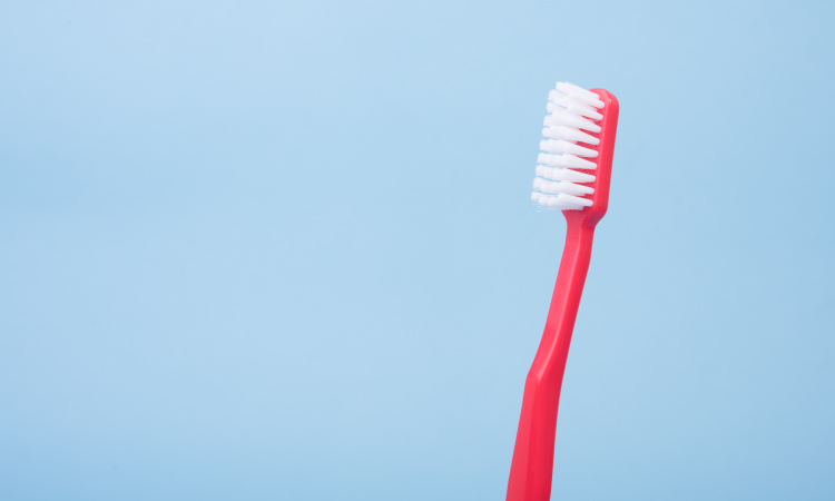 Red old toothbrush with white bristles against a powder blue background