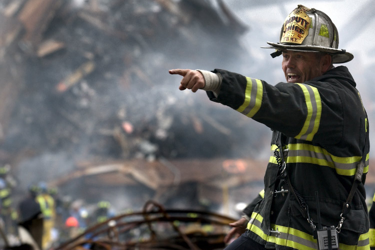 A firefighter in front of a pile of rubble points his finger instructing someone what to do after a fire or earthquake