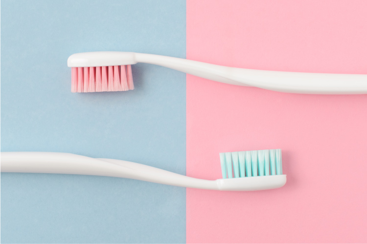 A pink bristled toothbrush and blue bristled toothbrush on a purple and pink background