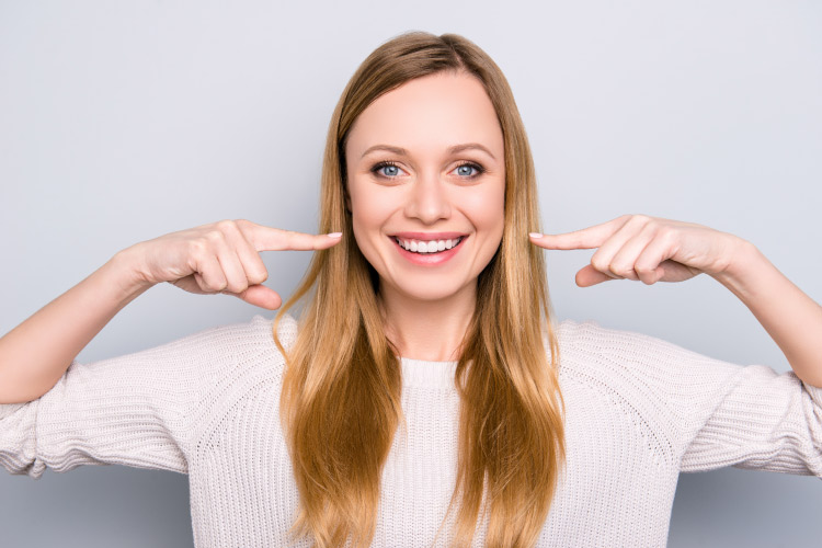 Blonde woman smiles and points to her smile with strong tooth enamel