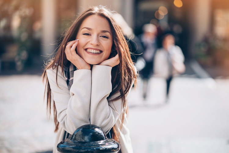 Brunette woman with ceramic braces smiles white in a city square