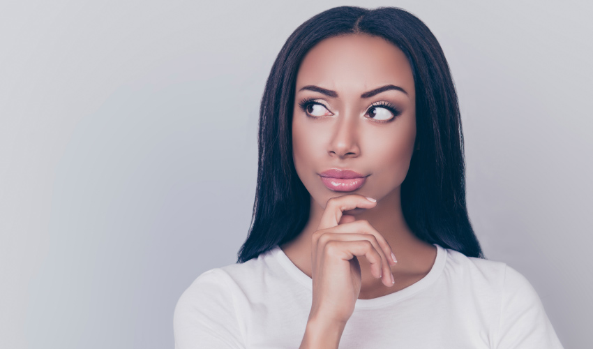 Dark-haired woman ponders her gum disease against a gray wall