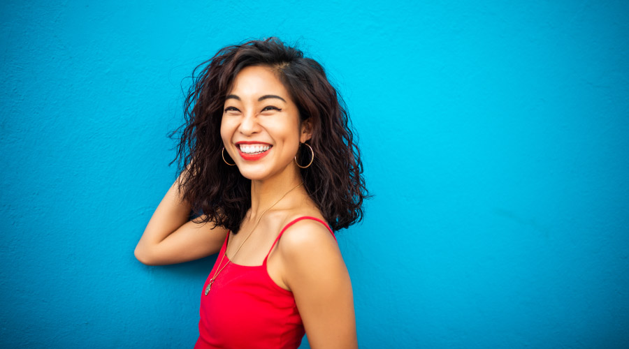 Brunette woman in a red tank top smiles against a blue wall after Six Month Smiles