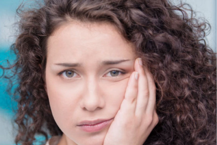 young woman holds her jaw in pain after wisdom tooth removal