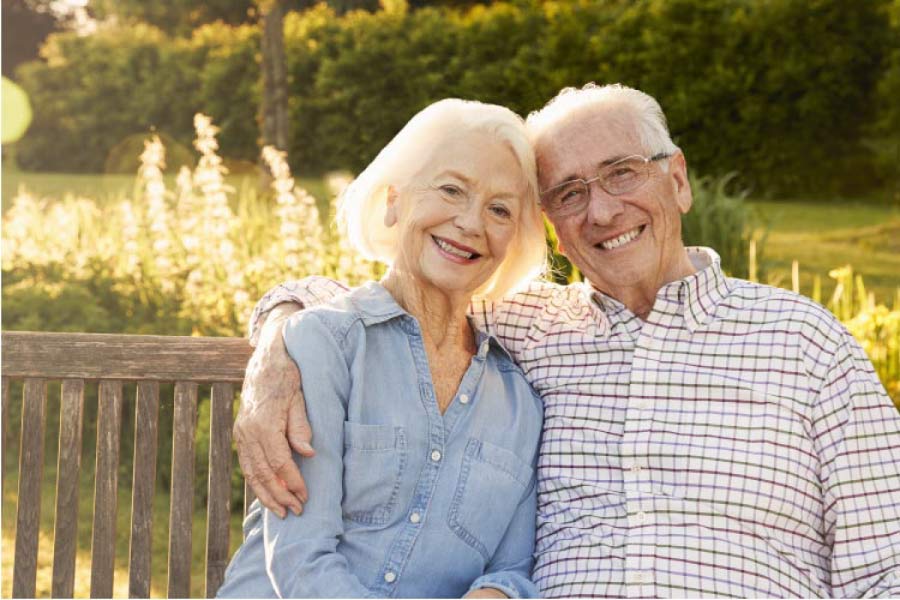 senior couple sitting on a bench hug and smile after learning about dental bridges