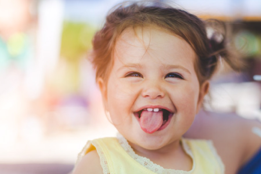 baby girl sticks out her tongue showing off two front baby teeth