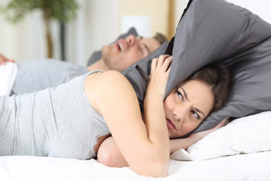 woman covers her ears with a pillow to block out her partners sleep apnea induced snoring