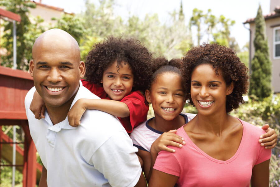 A mom and dad give their kids piggy back rides before visiting their family dentist at CarolinasDentist