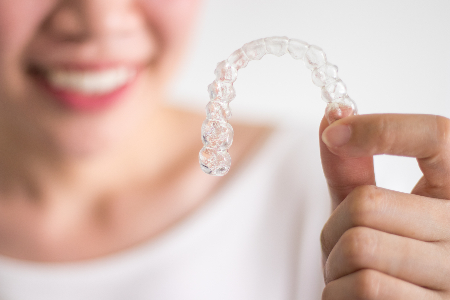 A blurry woman holds up her Invisalign aligner in the forefront