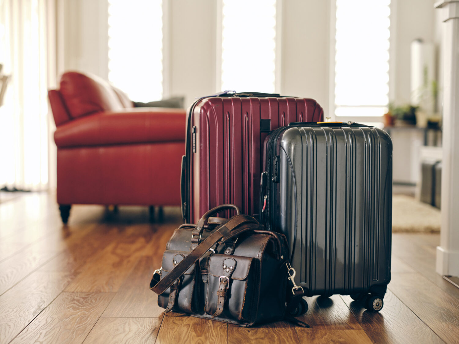 2 hard-sided suitcases next to a leather overnight bag in a living room packed to go on a trip