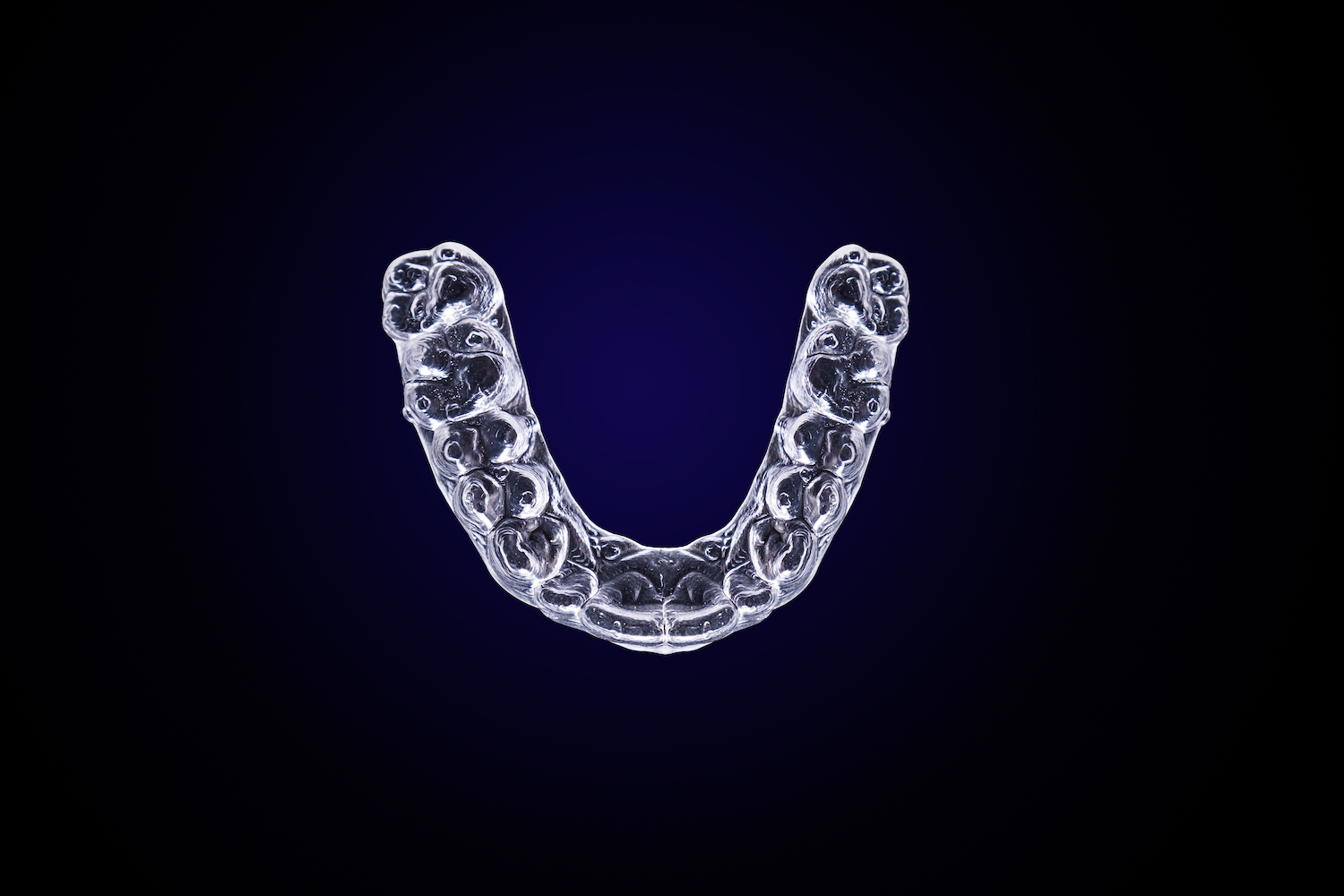 Aerial view of clear Invisalign aligners on a dark blue background