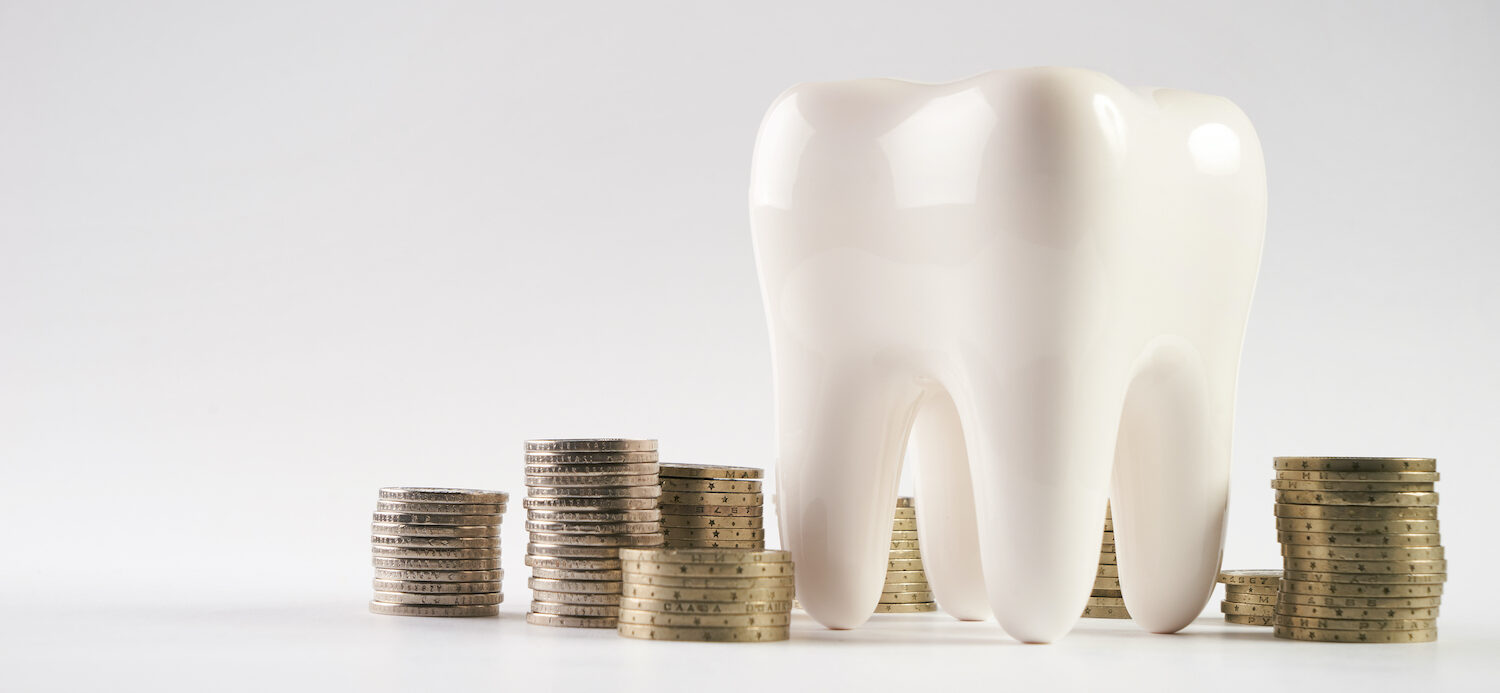 A large white tooth next to stacks of coins