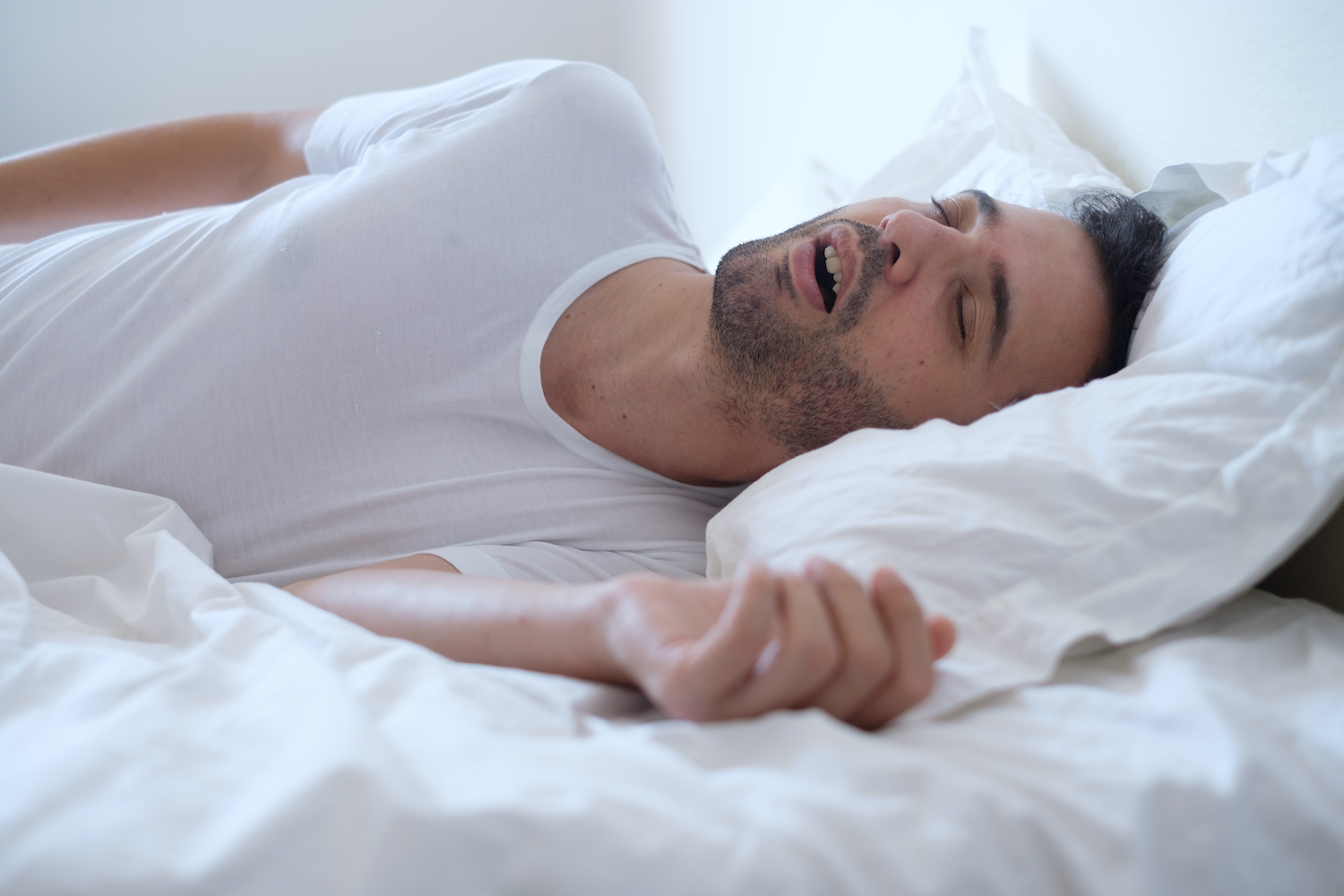 A brunette white man with obstructive sleep apnea snores while sleeping in his bed