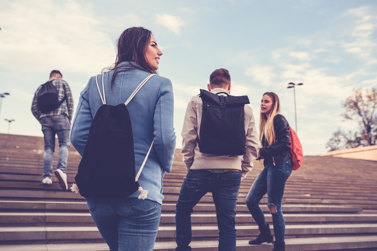 4 college kids with backpacks walk up a wide staircase as they go to their next class