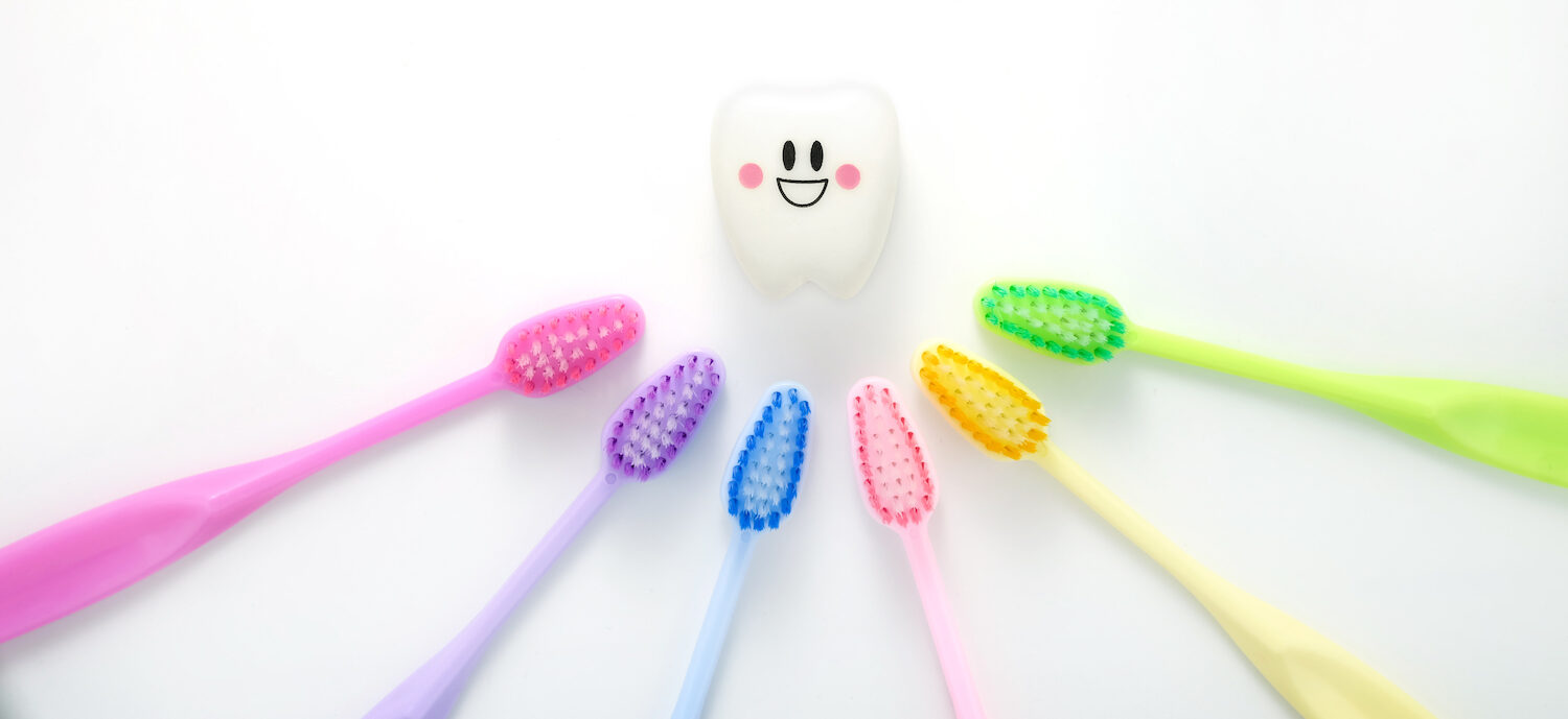 A rainbow of toothbrushes surround a smiling tooth for a blog post about choosing the right dentist