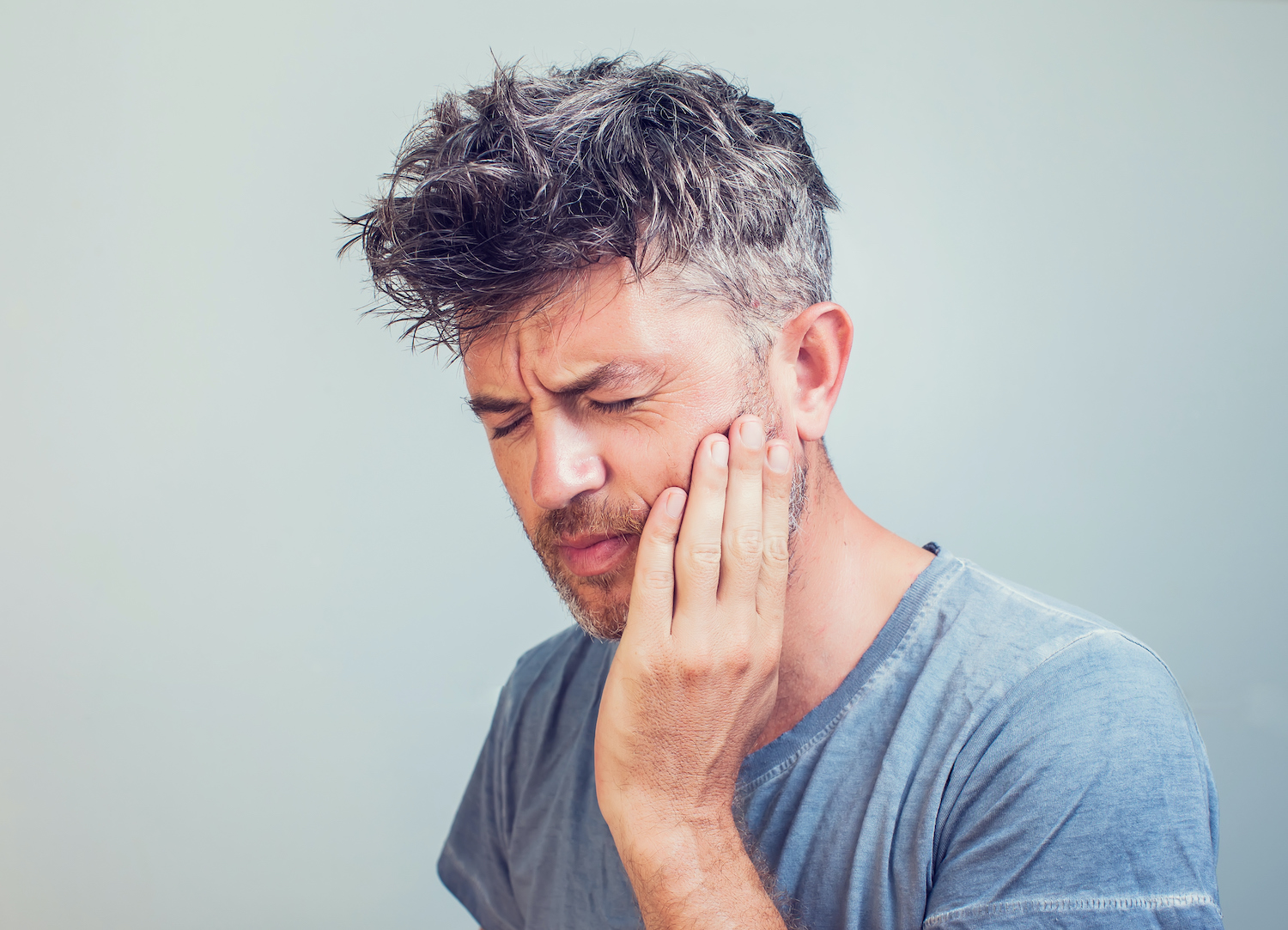 Middle-age white man with a compromised filling touches his cheek due to tooth sensitivity