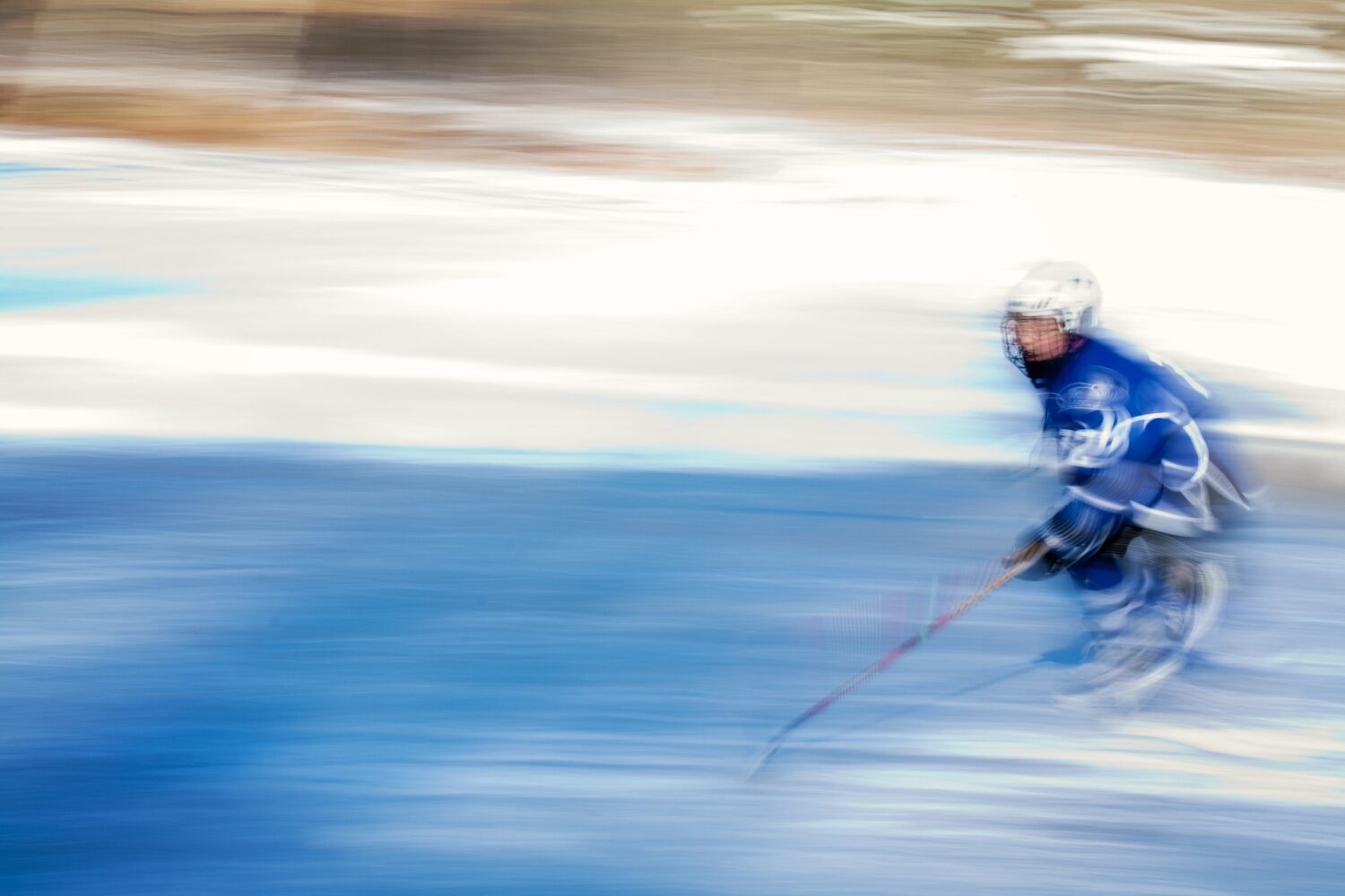 Artistically blurry image of an athlete playing ice hockey on a rink while wearing a blue jersey and helmet