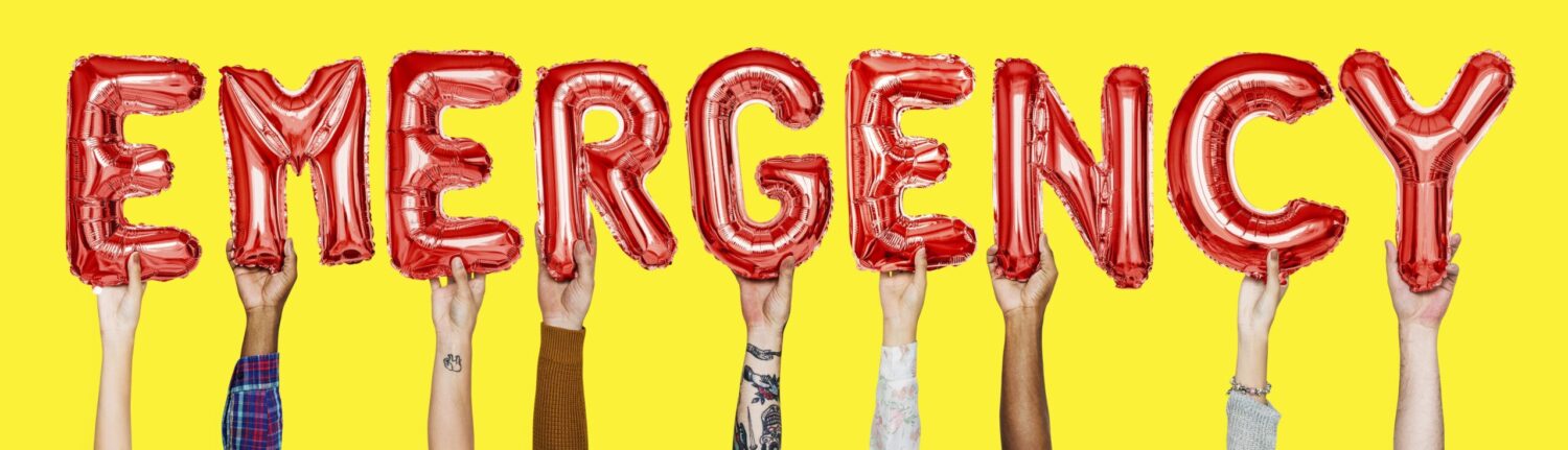 Hands hold up red balloon letters that say EMERGENCY against a yellow background