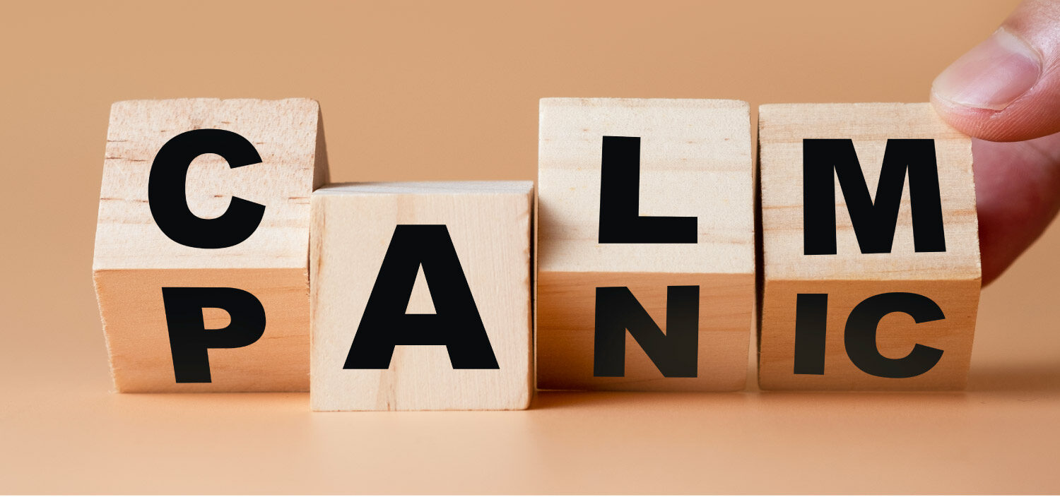 Wooden letter blocks being turned from PANIC to CALM against a tan background