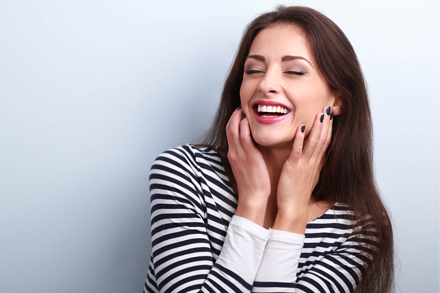 Brunette woman in a striped shirt smiles with a bright white smile after cosmetic dentistry