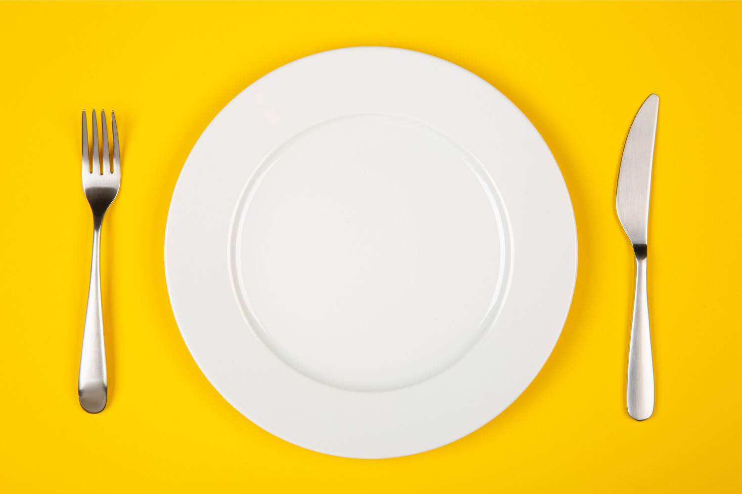 Aerial view of a white plate on a yellow table next to silverware